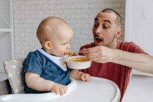 cute child being fed by joyful father-healthy eating