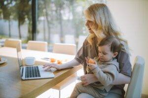 mom working while baby sitting on her lap eating orange-eco-friendly parenting-postpartum