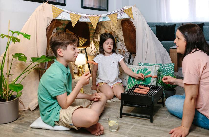 Fun Rainy Day Indoor Activities to Delight Your Kids 2 Family grilling and eating sausages on barbecue while camping at home-indoor